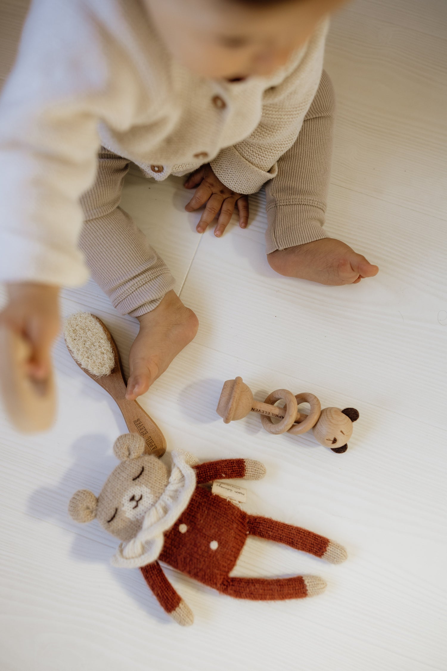 Bébé assis au sol avec doudou ourson et hochet en bois en forme d'ours