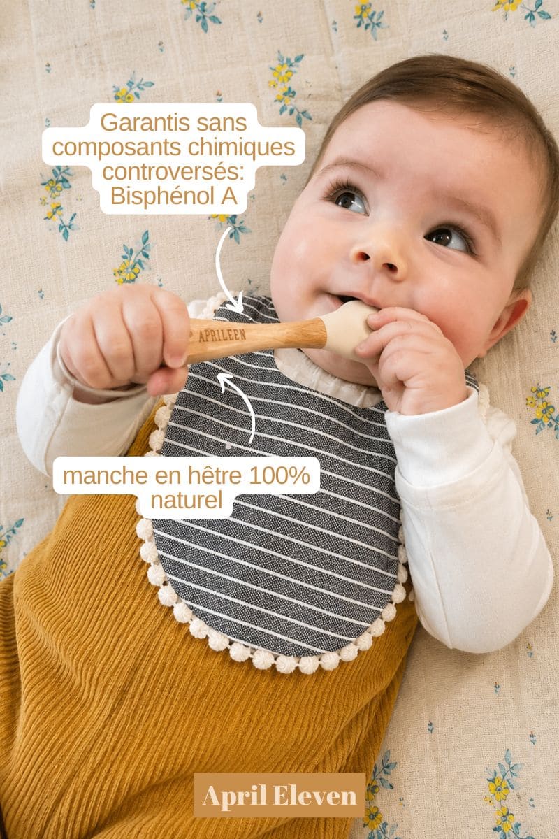 Bébé allongé sur le dos avec bavoir et cuillère en silicone et bois dans les mains
